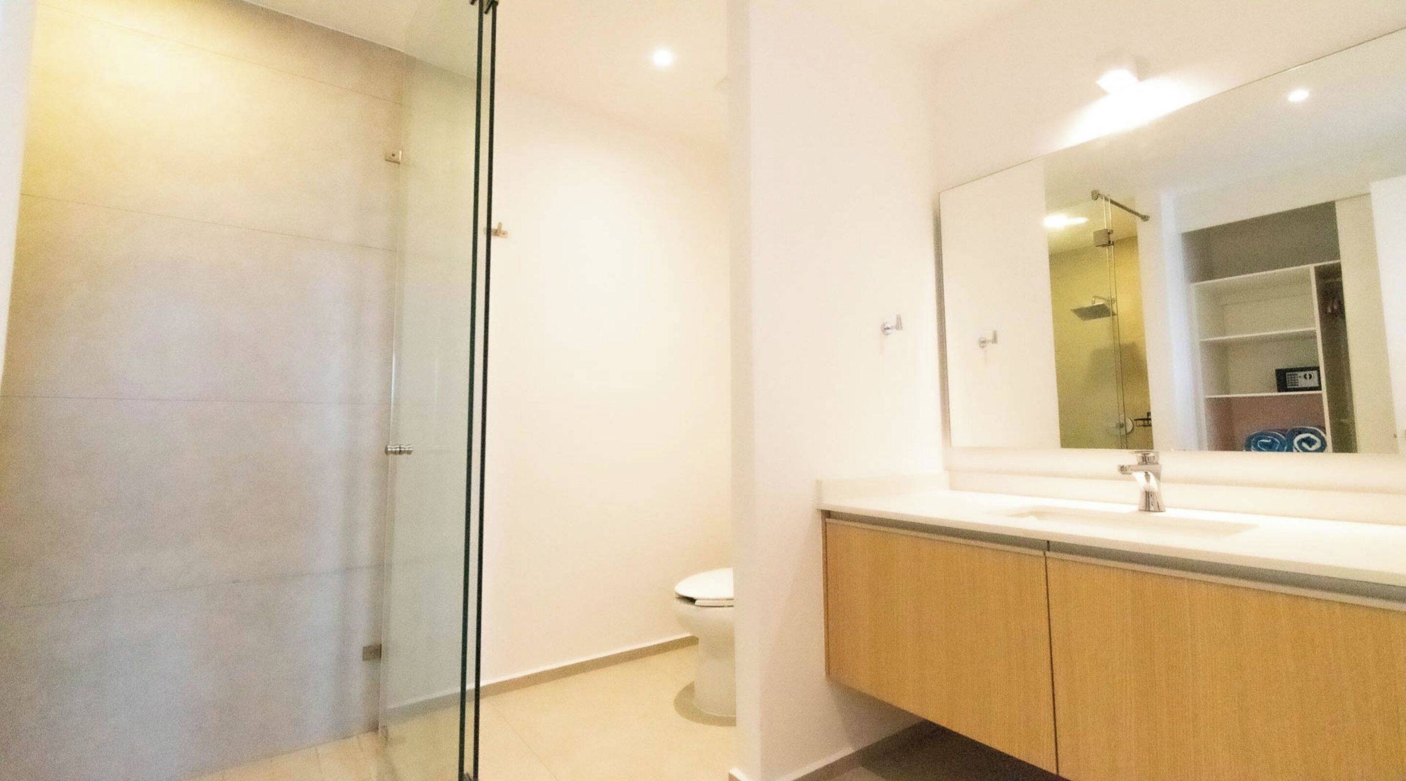 Un baño moderno con cabina de ducha de vidrio, inodoro blanco y un espejo grande sobre un lavabo con muebles de madera.