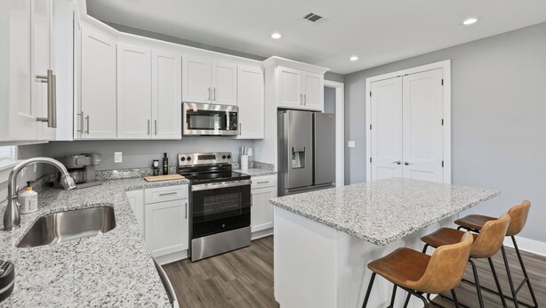 A modern kitchen with white cabinets, stainless steel appliances, granite countertops, and a bar area with stools. - Cozy 3BR Home - Fire Pit & Gated Parking in Midtown - Near Rhodes College & Zoo (Memphis)