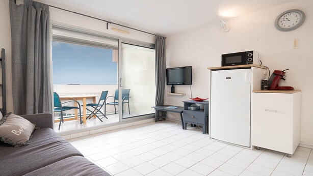 Ein moderner Wohnraum mit Balkon, Flachbildfernseher, Mikrowelle, Kaffeemaschine und Kühlschrank.