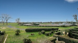 Ein angelegter Garten mit einem Heckenlabyrinth in Kreisform, einem Parkplatz mit Autos und blauem Himmel.