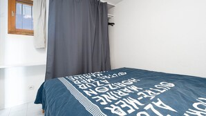 Ein Schlafzimmer mit Bett, grauen Vorhängen, einem Fenster und einer weißen Wand.