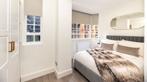 Une chambre à coucher avec un lit, un grand miroir et une vue sur un immeuble par la fenêtre.