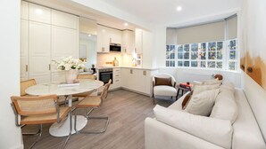 Une cuisine moderne avec des meubles blancs, une table à manger avec des chaises et une grande fenêtre donnant sur les arbres.