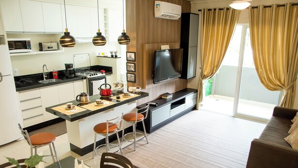 Eine moderne Küche mit einer zentralen Kochinsel, einem Essbereich mit Tisch für zwei Personen und einem Wohnbereich mit Sofa und Fernseher.