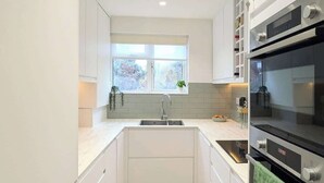Eine moderne Küche mit weißen Schränken, Holzboden, einem Fenster mit Aussicht und einem eingebauten Backofen.