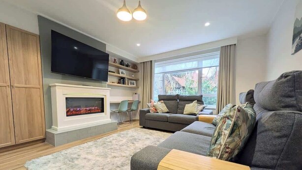 Ein modernes Wohnzimmer mit Kamin, einem grauen Sofa, einem Fernseher und einem großen Fenster.