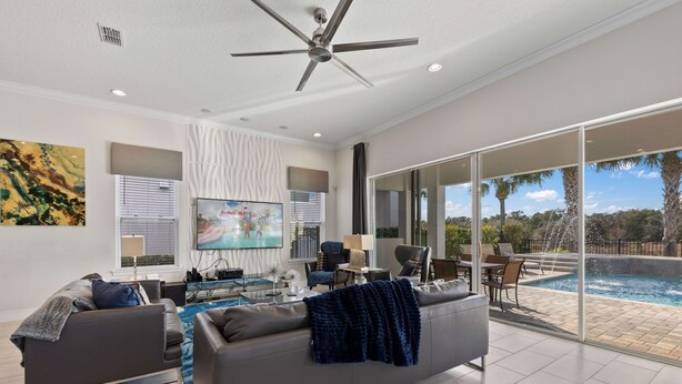 Ein modernes Wohnzimmer mit einem grauen Sofa, einem Couchtisch und einem Fernseher. Es gibt einen Balkon mit einem Pool und Palmen.