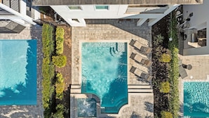 Ein Poolbereich auf dem Dach mit drei separaten Pools, umgeben von Liegestühlen und Pflanzen.