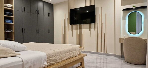 Een slaapkamer met een bed, een aan de muur bevestigde televisie, een kledingkast en een spiegel met groene lijst.