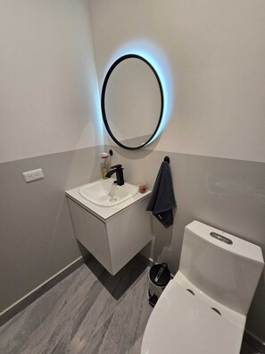 Een moderne badkamer met een witte wastafel, een zwarte kraan en een ronde spiegel met blauwe verlichting.