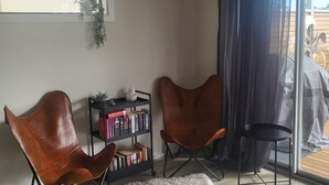 Ein Eckzimmer mit zwei braunen Ledersesseln, einem kleinen weißen Teppich, einem Bücherregal voller Bücher und einem Fenster mit einer Pflanze.