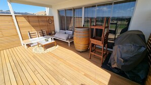 Eine Terrasse mit Holzboden, einem weißen Sofa, einem kleinen Tisch mit Pflanze, einem Holzbottich und einem Stuhl.