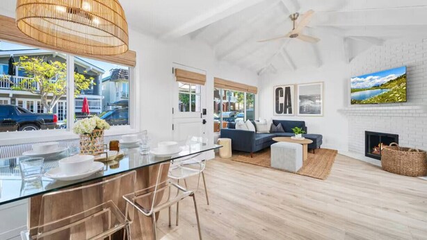 Een moderne keuken met een glazen eiland, een eethoek met stoelen, een woonkamer met een bank en een open haard, en een groot raam met uitzicht op de straat.