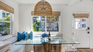 Een moderne keuken met een glazen eettafel, transparante stoelen en een rieten hanglamp.