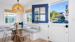 Een moderne keuken met een glazen eettafel, transparante stoelen, een raam met blauwe lijst en een witte deur.