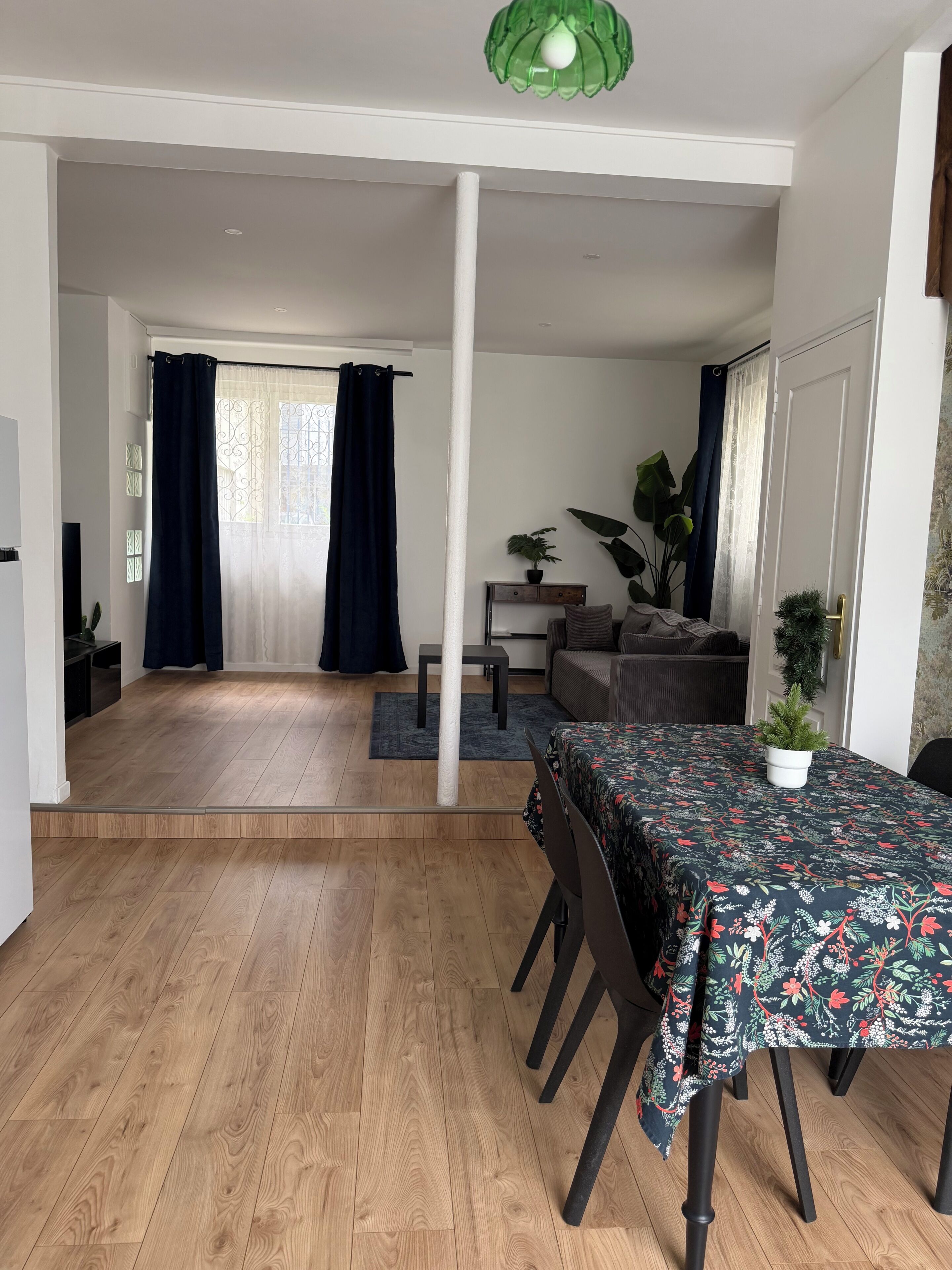 A dining area with a table set for four, a sofa, a potted plant, and a view into another room.