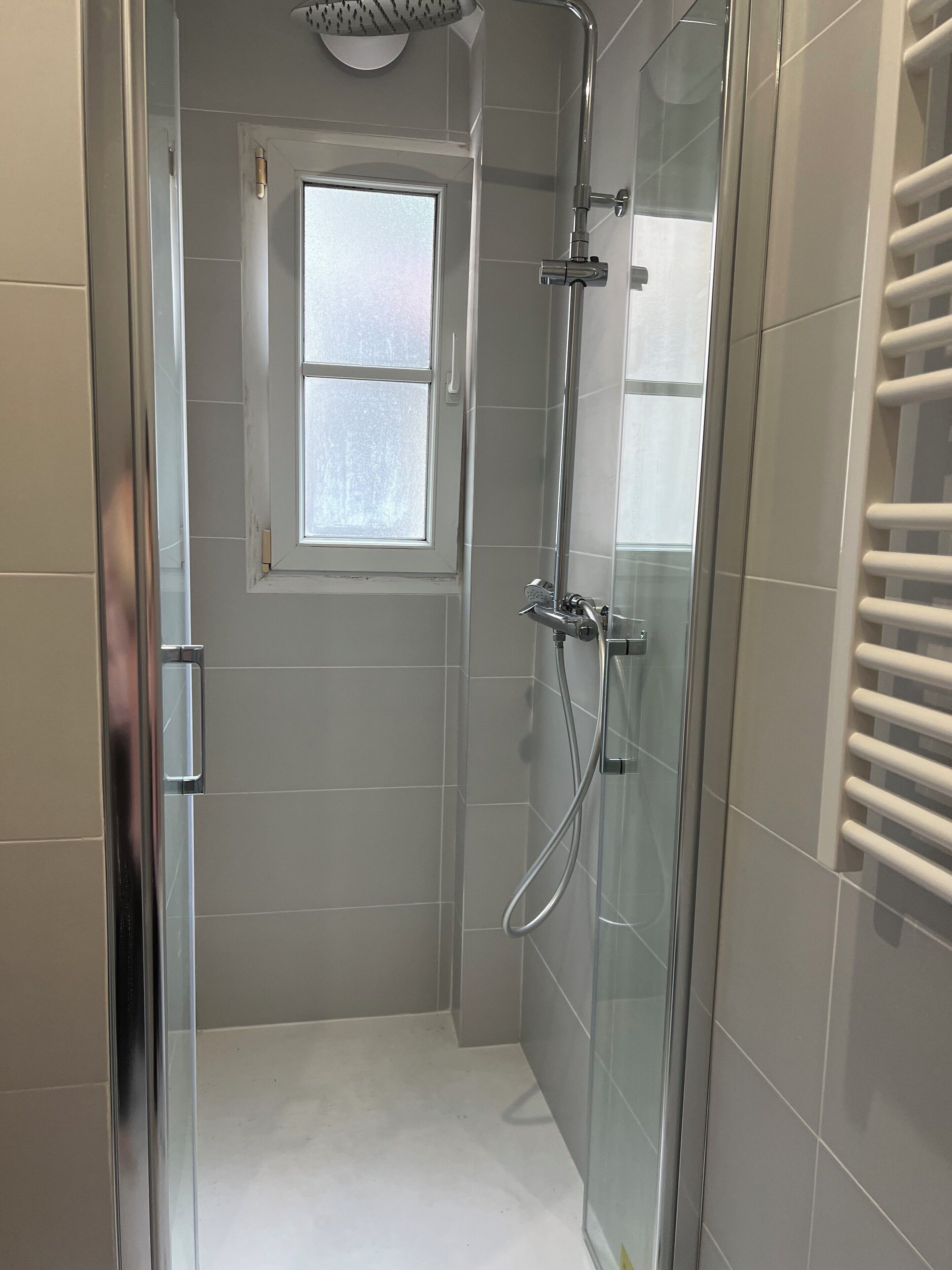 Une douche moderne avec une porte en verre, une fenêtre située au-dessus de la douche et un porte-serviettes sur la droite.