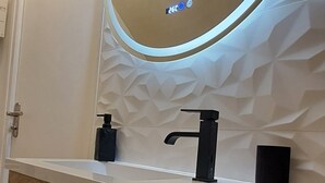 A bathroom with a wooden vanity, a round mirror with a light, and a towel rack. - Studio Notre Dame 3 in the heart of town, 30 minutes from the Puy du Fou park (Cholet)