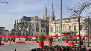 A cathedral with Gothic architecture, a plaza with red umbrellas, and potted plants. - Studio Notre Dame 3 in the heart of town, 30 minutes from the Puy du Fou park (Cholet)