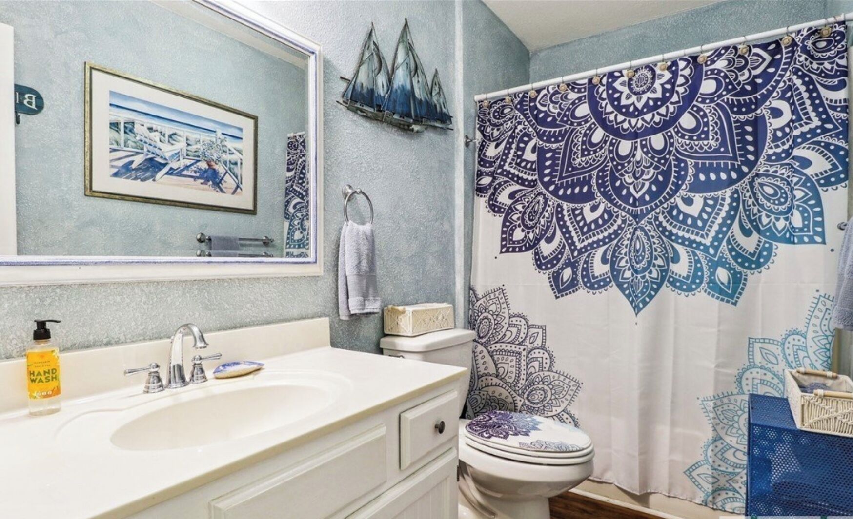 Et badeværelse med vask, toilet og bruseforhæng med blåt paisley-mønster.