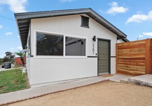 Una casa moderna de un piso con fachada blanca, puerta verde y valla de madera.