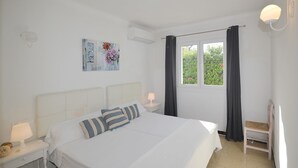A bedroom with a bed, a nightstand, a chair, a window with curtains, and wall art.