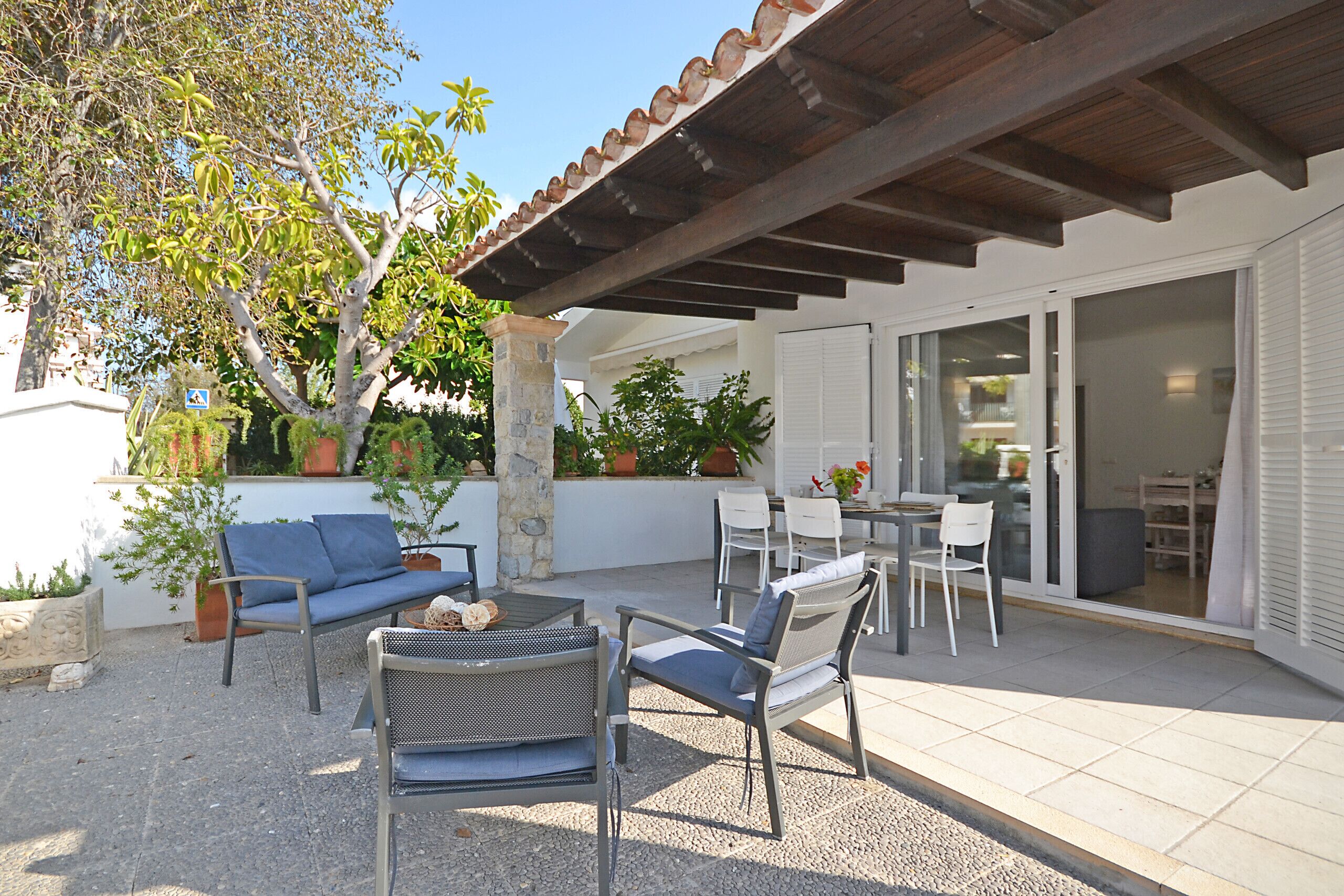 Un patio exterior con zona de estar cubierta, una mesa de comedor y un ventanal grande.