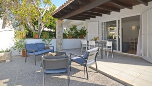 An outdoor patio with a covered seating area, a dining table, and a large window.