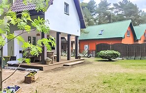 A residential area with a white house, a red house, and a green roof. There is a small bush and a wooden structure in the yard.