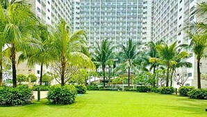 A well-maintained courtyard with a lawn, surrounded by tall buildings and palm trees. - Live Just Steps Away From Mall of Asia (Pasay)