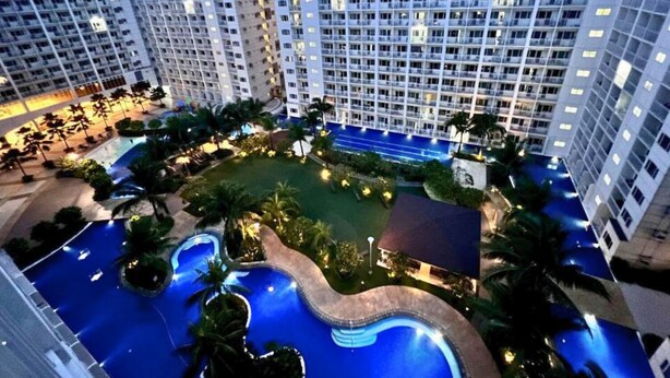 A high-rise hotel with multiple floors, a central courtyard with a swimming pool, and surrounding greenery. - Live Just Steps Away From Mall of Asia (Pasay)