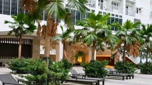 A hotel lobby with palm trees, lounge chairs, and a modern building facade. - Live Just Steps Away From Mall of Asia (Pasay)