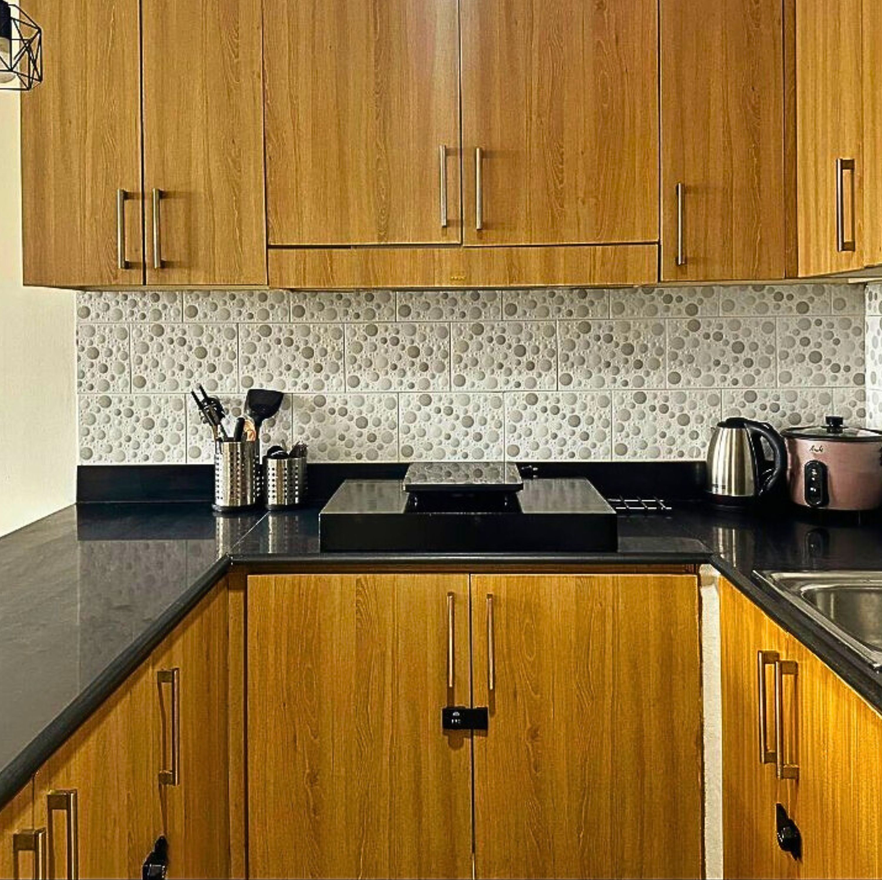 Cocina con armarios de madera, encimera negra y salpicadero con diseños circulares.