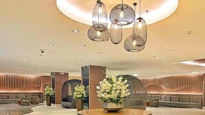 A modern lobby with a central seating area, a round table with a floral centerpiece, and hanging pendant lights. - Live Just Steps Away From Mall of Asia (Pasay)