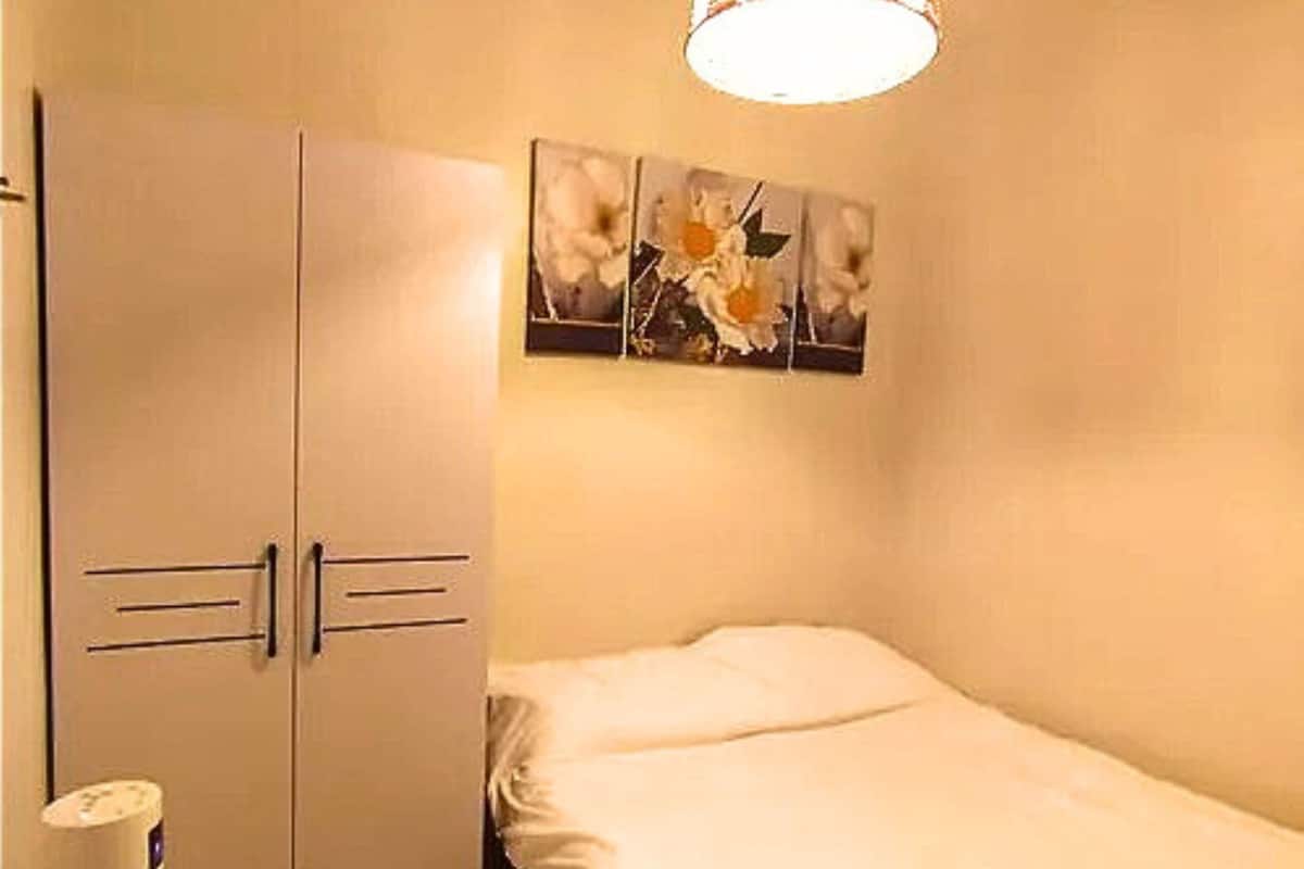 Een slaapkamer met een enkel bed, een kledingkast en een wandlamp.