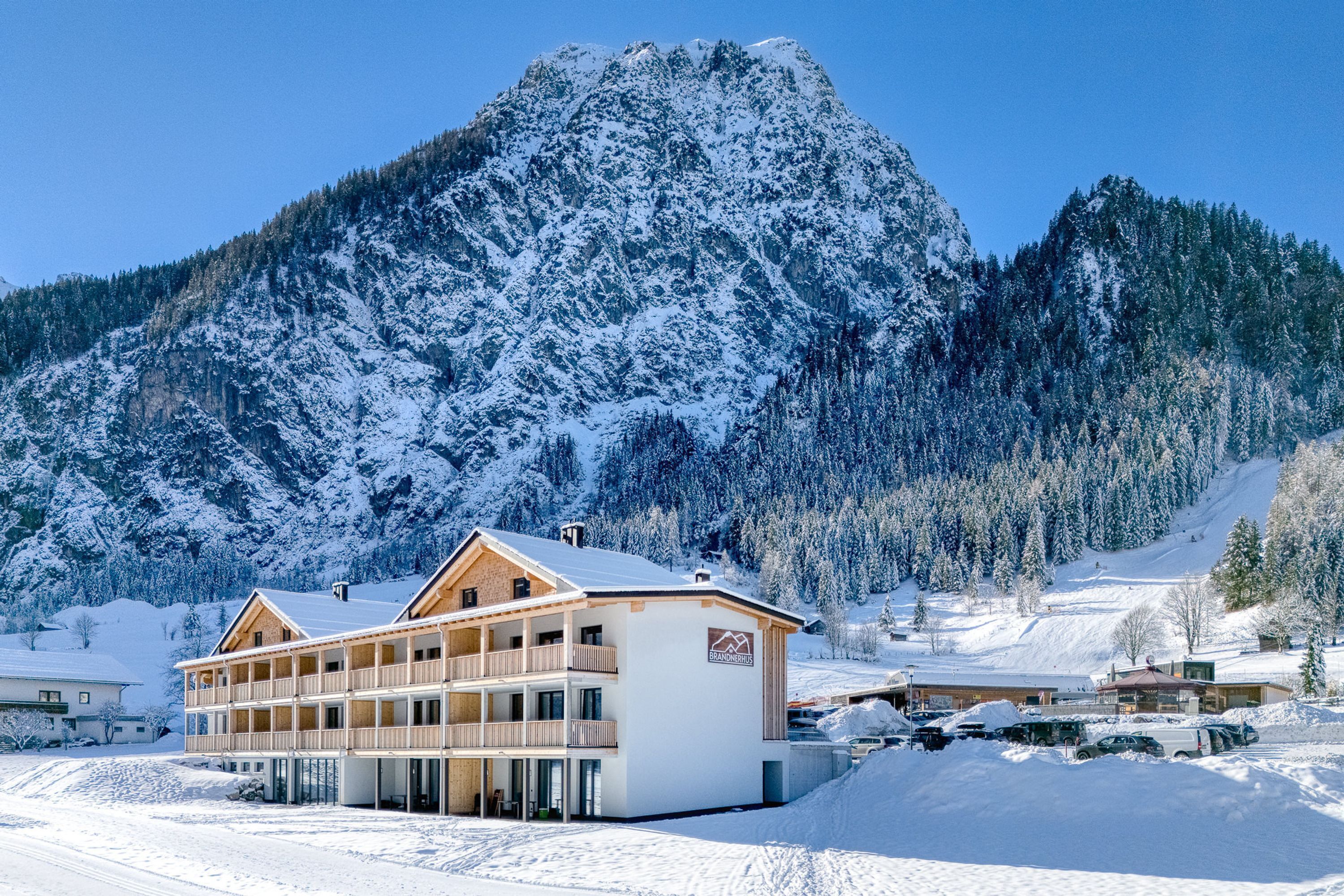 A multi-story building with balconies, surrounded by snow-covered mountains and trees.