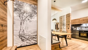 A modern kitchen with wooden cabinets, a dining area with a table and chairs, and a large wall mural of a tree and landscape.