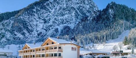 A multi-story building with balconies, surrounded by snow-covered mountains and trees.