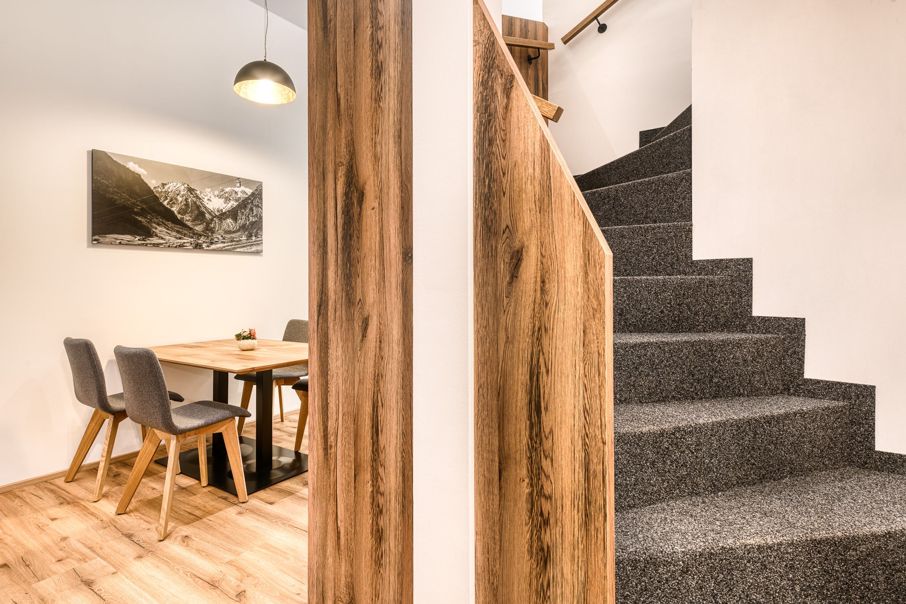 A modern interior with a wooden dining table, chairs, and a staircase with a wooden railing.