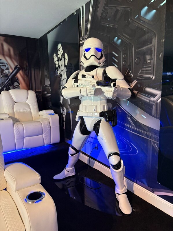 Una habitación con un sofá de cuero blanco acolchado, un mural de pared futurista y una figura de Stormtrooper.