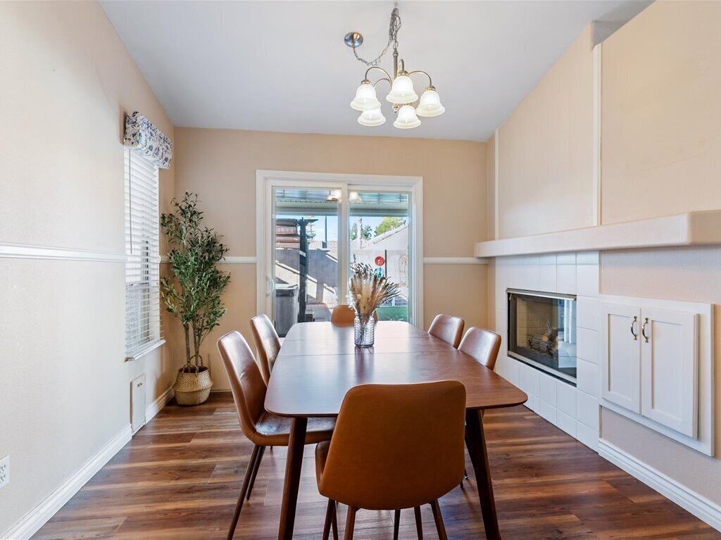 A dining area with a wooden table, chairs, a chandelier, a potted plant, and a fireplace.