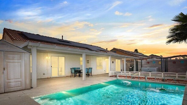A swimming pool with a tiled deck, a covered patio area with chairs, and a building with a tiled roof. - 3BD Pool+Jacuzzi Oasis! (North Las Vegas)