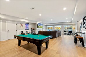 Ein Billardtisch in einem Raum mit Holzboden, einer Couch und einem Essbereich mit Stühlen.