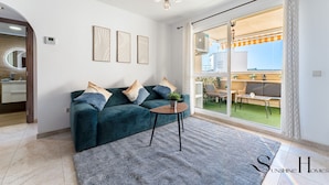 A modern living room with a teal sofa, a small round table, and a large sliding glass door leading to an outdoor patio.