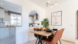 A modern kitchen with white cabinets, a wooden dining table with brown chairs, and a large window.