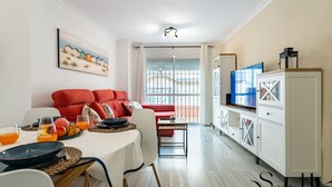 A modern living room with a red sofa, dining table with breakfast, and a TV on a cabinet. - 50 Meters from the Beach, 1 Bedroom with Parking REF013 (Torremolinos)