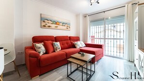 A modern living room with a red sofa, a small wooden table, and a painting on the wall. - 50 Meters from the Beach, 1 Bedroom with Parking REF013 (Torremolinos)