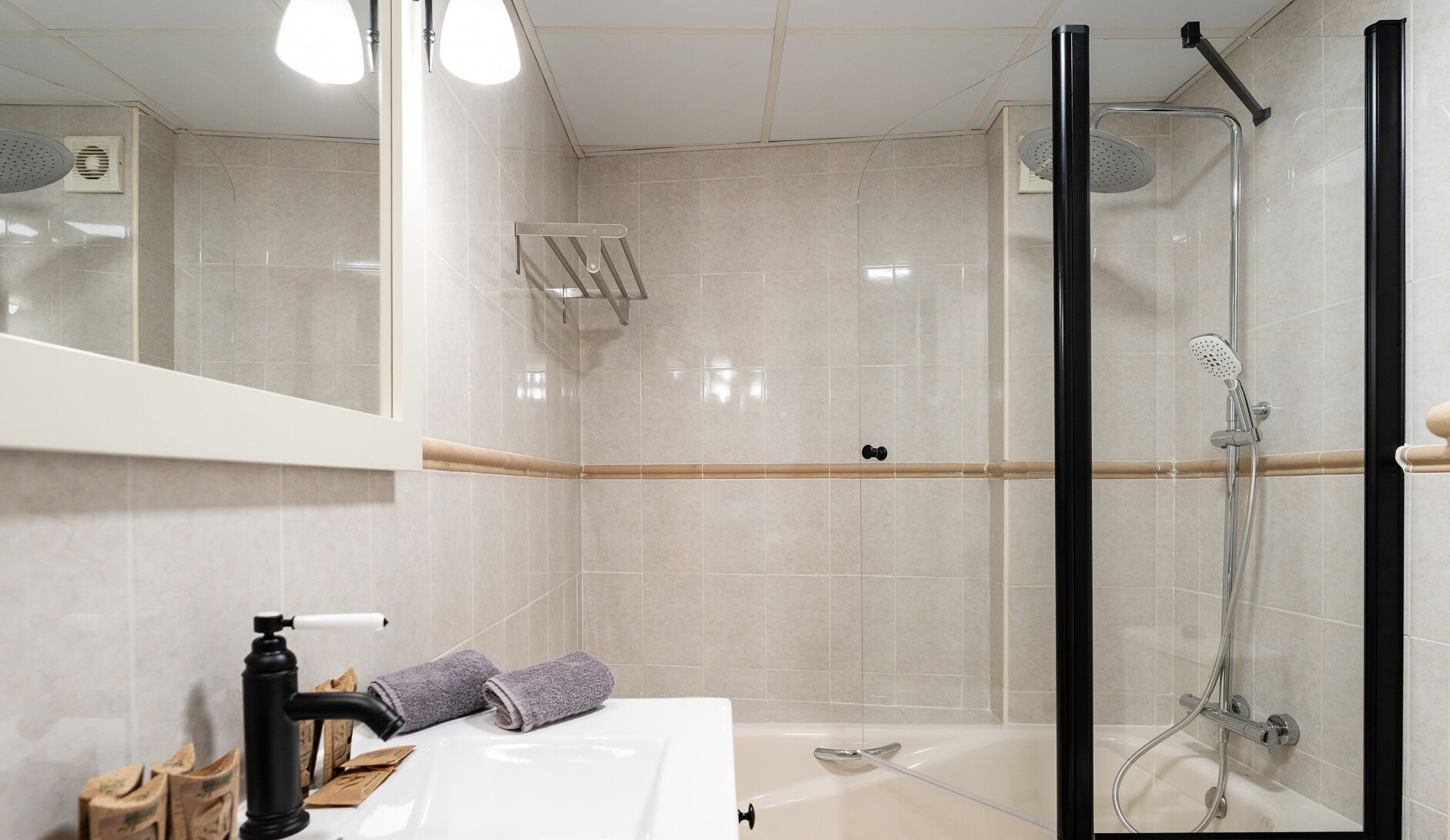 Een moderne badkamer met een douche met glazen wand, een witte wastafel en een spiegel boven de wastafel.