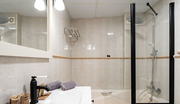 Ein modernes Badezimmer mit einer Duschkabine, einem weißen Waschbecken und einem Spiegel darüber.
