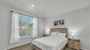 Un dormitorio con cama, dos mesitas de noche, una ventana con cortinas y decoración en la pared.